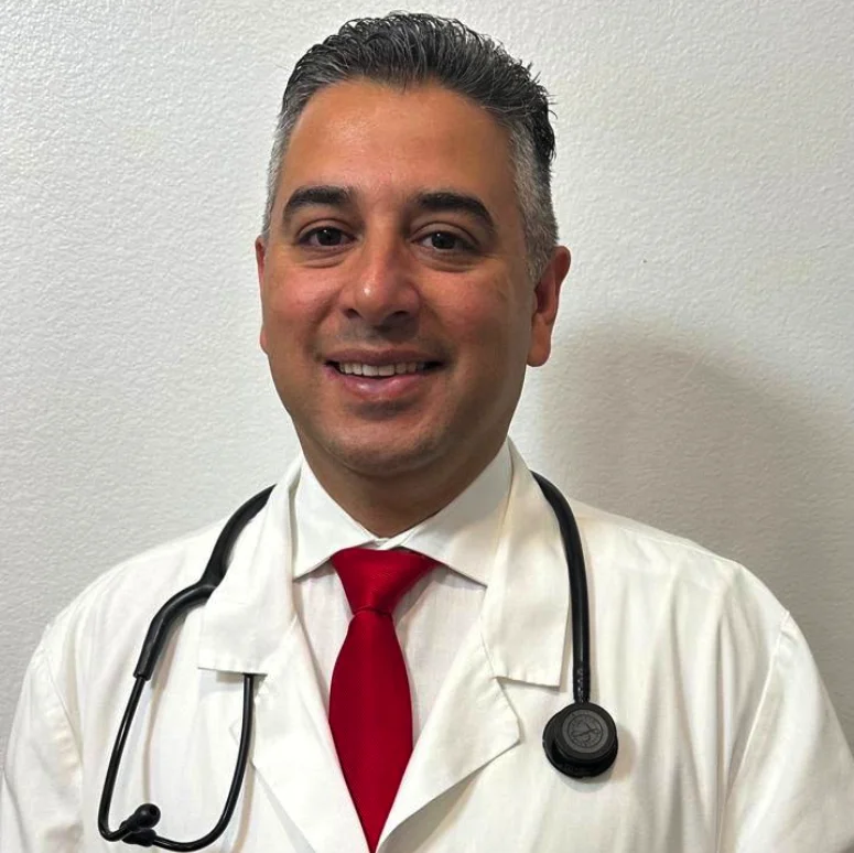 Dr. Mousa, a smiling physician in a white coat and red tie